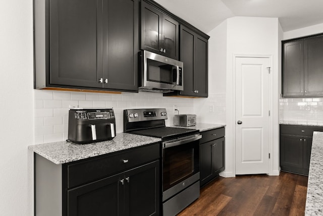 kitchen featuring dark cabinets, stainless steel appliances, dark wood-style flooring, light stone countertops, and tasteful backsplash