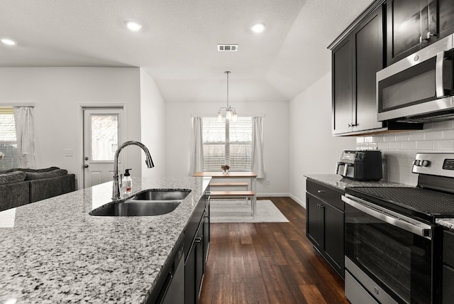 kitchen with stainless steel appliances, a sink, backsplash, light stone countertops, and decorative light fixtures