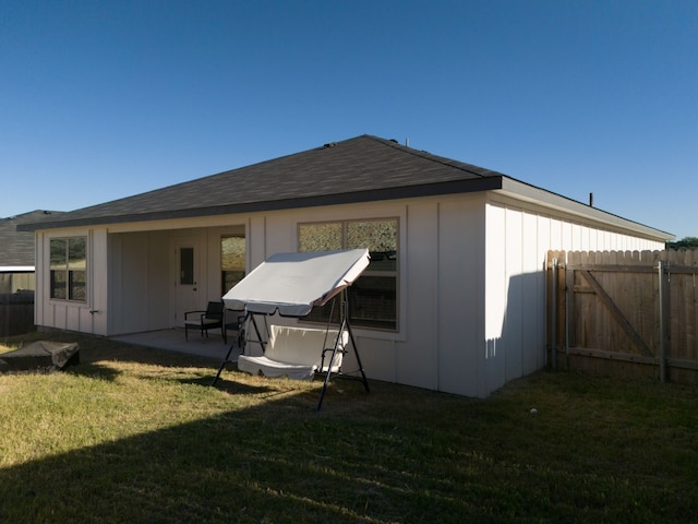 back of house with board and batten siding, a lawn, fence, and a patio