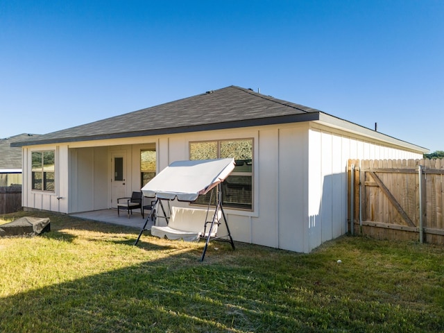 rear view of house with a patio, a lawn, board and batten siding, and fence