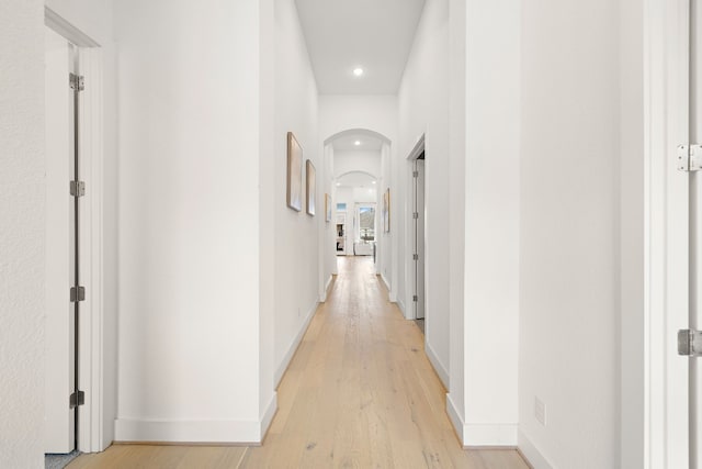 corridor with recessed lighting, arched walkways, light wood finished floors, and baseboards
