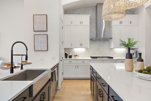 kitchen with wall chimney range hood, white cabinets, light countertops, a sink, and stainless steel appliances