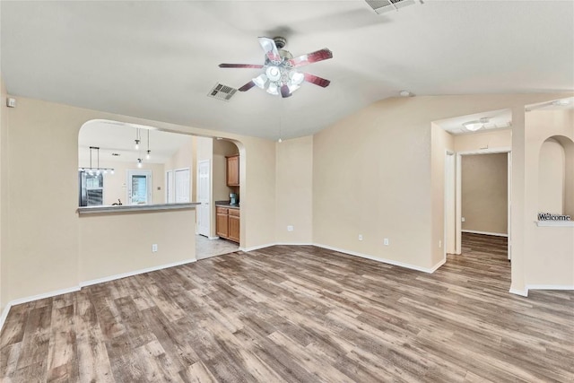 unfurnished living room featuring arched walkways, lofted ceiling, wood finished floors, visible vents, and a ceiling fan