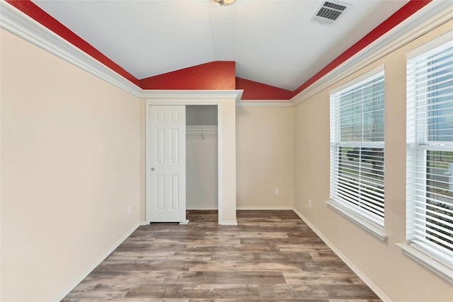 unfurnished bedroom featuring lofted ceiling, wood finished floors, visible vents, baseboards, and a closet