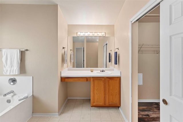 full bath with a walk in closet, vanity, baseboards, and a bath