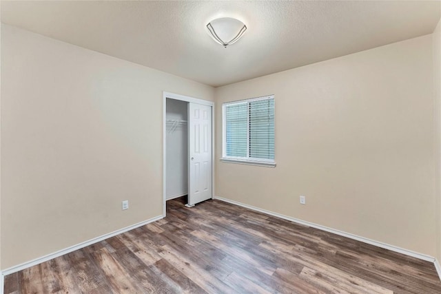 unfurnished bedroom with dark wood-style floors, a textured ceiling, baseboards, and a closet