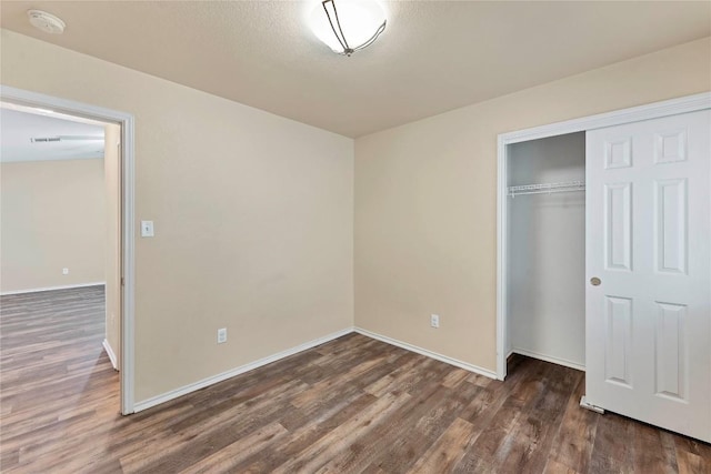 unfurnished bedroom featuring a closet, dark wood finished floors, and baseboards