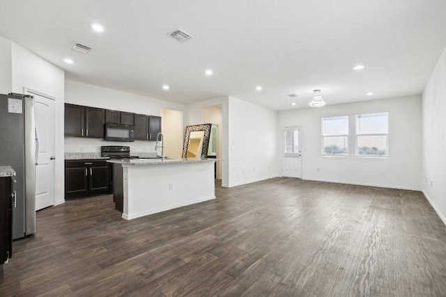 kitchen with black microwave, visible vents, open floor plan, freestanding refrigerator, and an island with sink