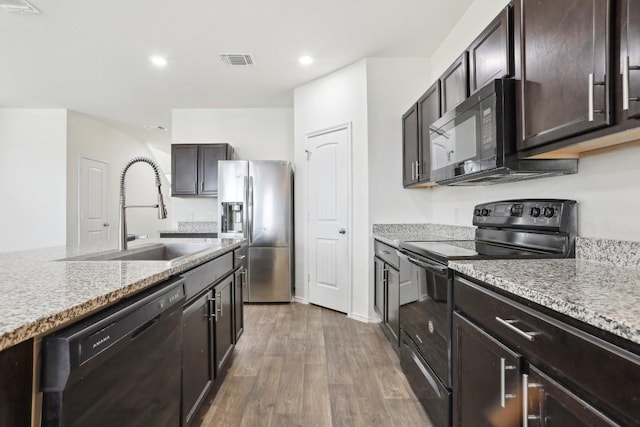 kitchen with dark brown cabinetry, wood finished floors, visible vents, a sink, and black appliances