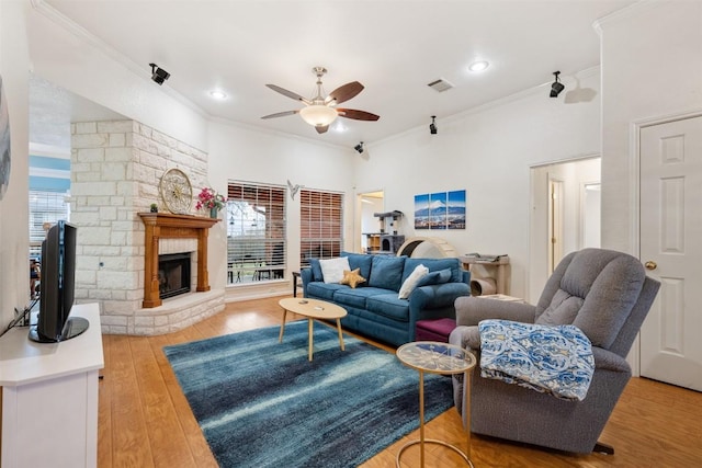 living area featuring crown molding, visible vents, a ceiling fan, a stone fireplace, and wood finished floors