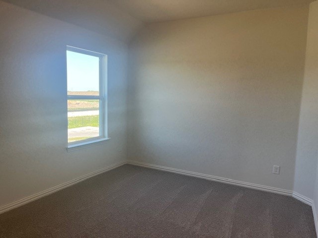 empty room featuring vaulted ceiling, baseboards, and dark carpet