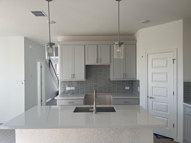kitchen with tasteful backsplash, visible vents, a sink, a kitchen island with sink, and gray cabinets