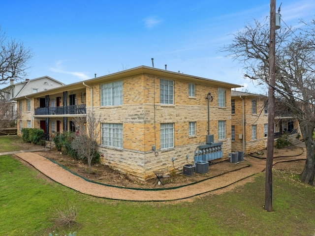 back of house featuring central AC, brick siding, a yard, and a balcony