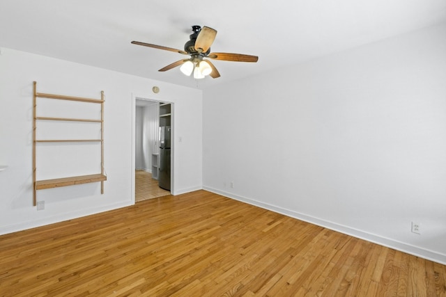 spare room featuring light wood-type flooring, a ceiling fan, and baseboards