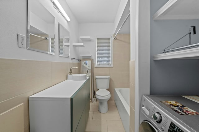 bathroom featuring toilet, washer / clothes dryer, tile patterned floors, vanity, and tile walls