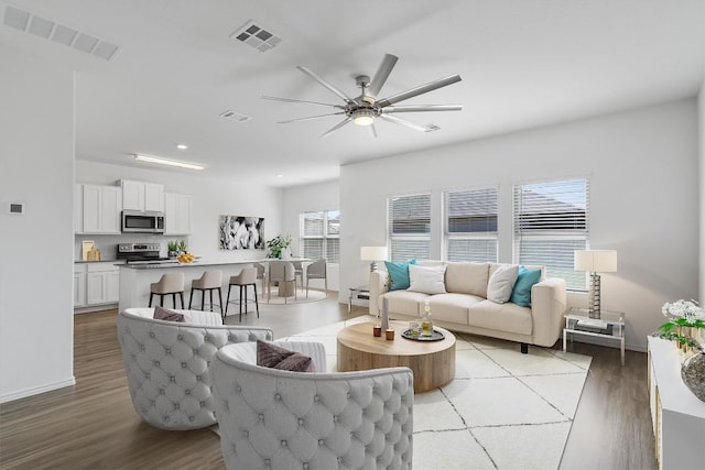 living room with a ceiling fan, visible vents, and wood finished floors