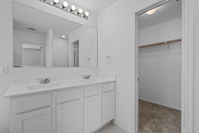 full bathroom with double vanity, visible vents, a walk in closet, and a sink