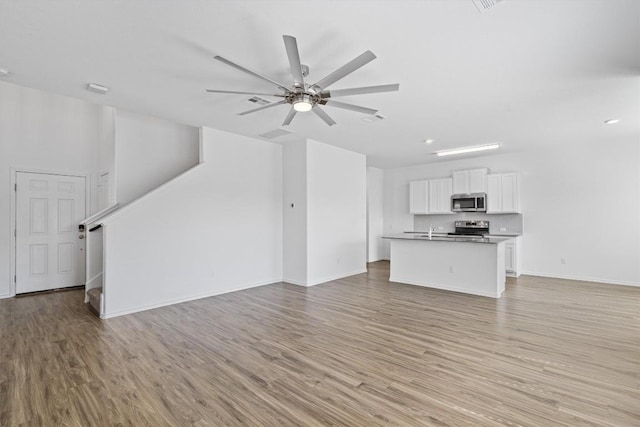 unfurnished living room with ceiling fan, stairway, baseboards, and light wood-style floors