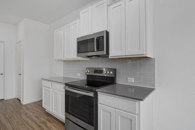 kitchen with white cabinets, dark countertops, stainless steel appliances, and wood finished floors