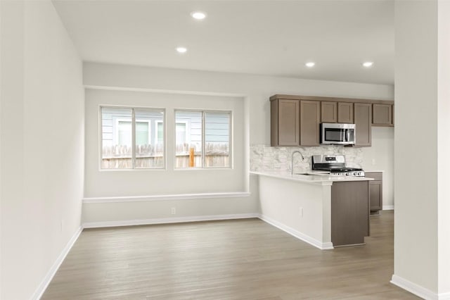 359 Witchhazel Way, San Marcos, TX 78666 - kitchen featuring stainless steel appliances, light countertops, light wood-style flooring, decorative backsplash, and a peninsula