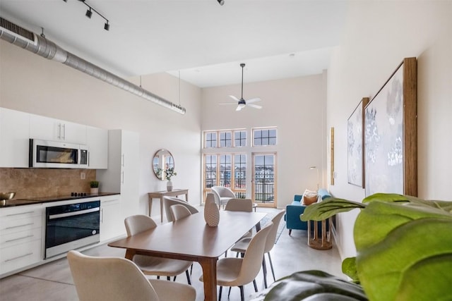 dining room featuring concrete floors, visible vents, a towering ceiling, a ceiling fan, and rail lighting