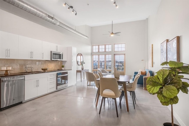 kitchen featuring stainless steel appliances, concrete floors, a sink, white cabinetry, and dark countertops