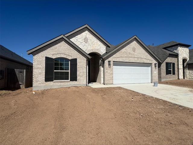 french provincial home featuring an attached garage, brick siding, and driveway