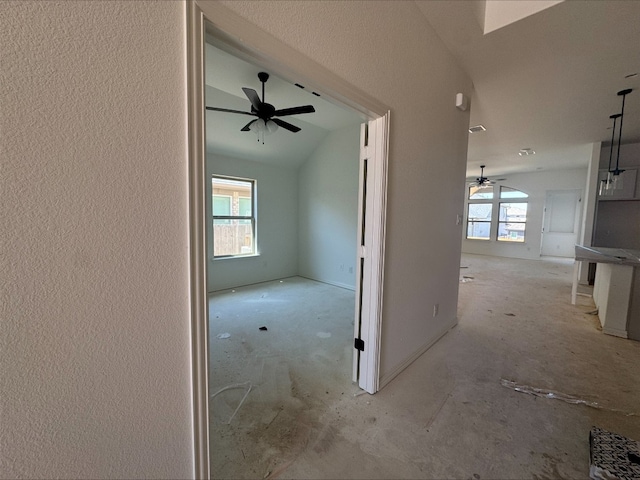 corridor featuring plenty of natural light, lofted ceiling, and a textured wall