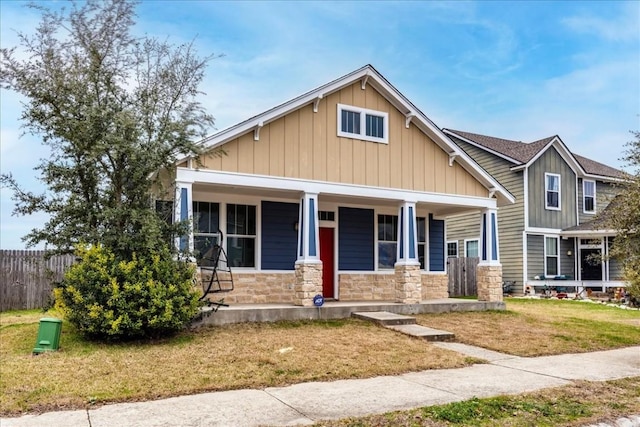 craftsman house with a porch, board and batten siding, a front yard, fence, and stone siding