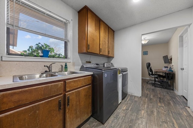 washroom featuring a textured ceiling, washing machine and clothes dryer, a sink, cabinet space, and dark wood finished floors