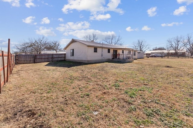 rear view of property featuring metal roof, a yard, brick siding, and a fenced backyard