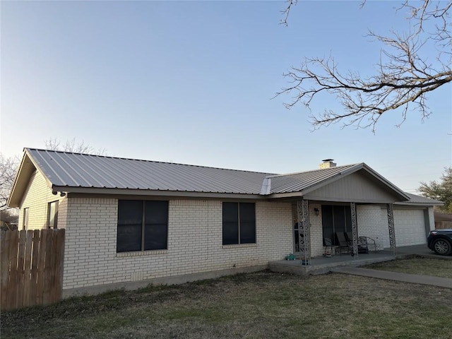 ranch-style home featuring brick siding, a front yard, metal roof, fence, and a garage