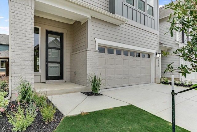 view of exterior entry featuring a garage, board and batten siding, concrete driveway, and brick siding