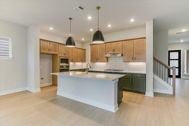 kitchen featuring stainless steel appliances, under cabinet range hood, light countertops, tasteful backsplash, and light wood-type flooring