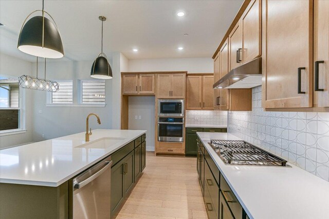 kitchen with stainless steel appliances, a sink, under cabinet range hood, light countertops, and light wood-type flooring