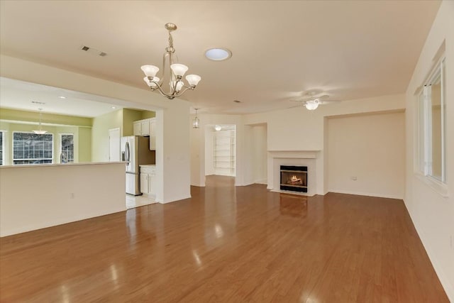 unfurnished living room featuring a fireplace with flush hearth, ceiling fan with notable chandelier, visible vents, and wood finished floors