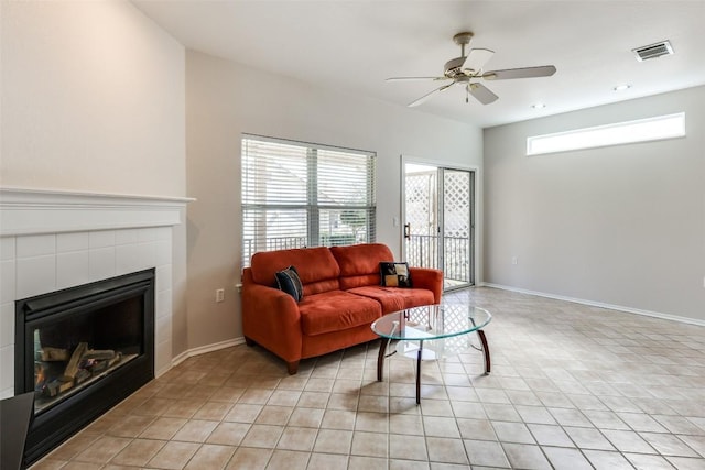 living area with light tile patterned floors, visible vents, a tiled fireplace, a ceiling fan, and baseboards