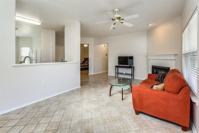 living area with baseboards, a ceiling fan, and a tiled fireplace