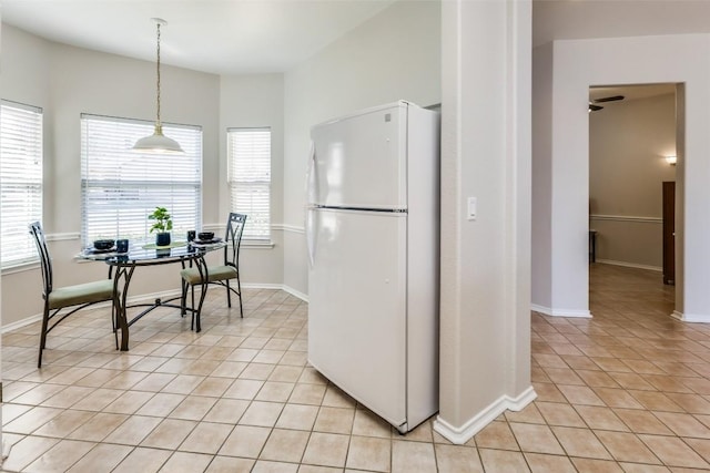 kitchen featuring light tile patterned floors, baseboards, freestanding refrigerator, and decorative light fixtures