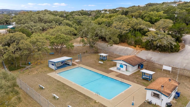 community pool with a patio area, an outdoor structure, fence, and a view of trees