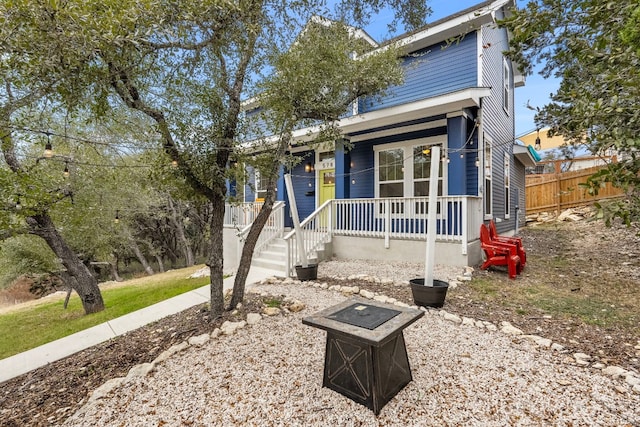 view of front of property featuring covered porch, an outdoor fire pit, and fence