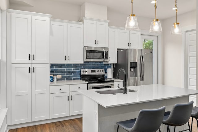 kitchen featuring pendant lighting, appliances with stainless steel finishes, a kitchen island with sink, white cabinets, and a sink