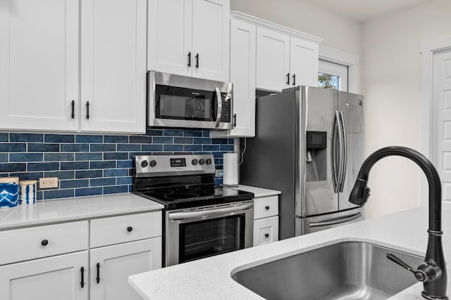 kitchen with tasteful backsplash, white cabinets, light stone counters, stainless steel appliances, and a sink