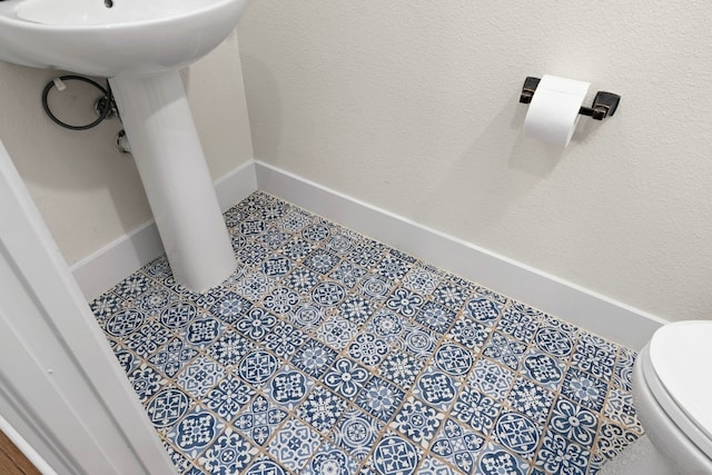 half bath featuring baseboards, toilet, and tile patterned floors