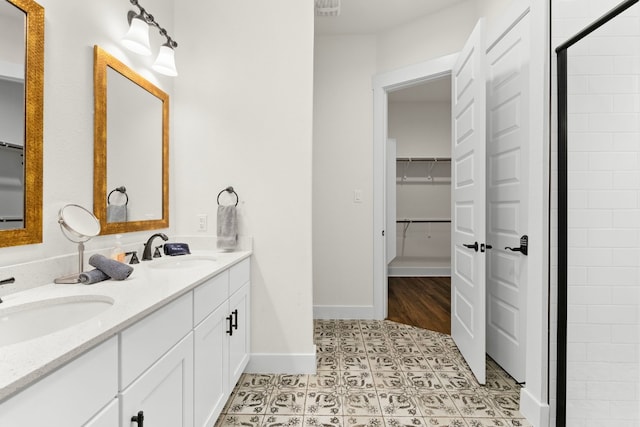 bathroom featuring double vanity, a spacious closet, a sink, and baseboards