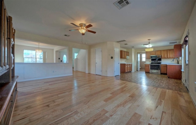 unfurnished living room featuring ceiling fan, light wood-style flooring, a sink, and visible vents