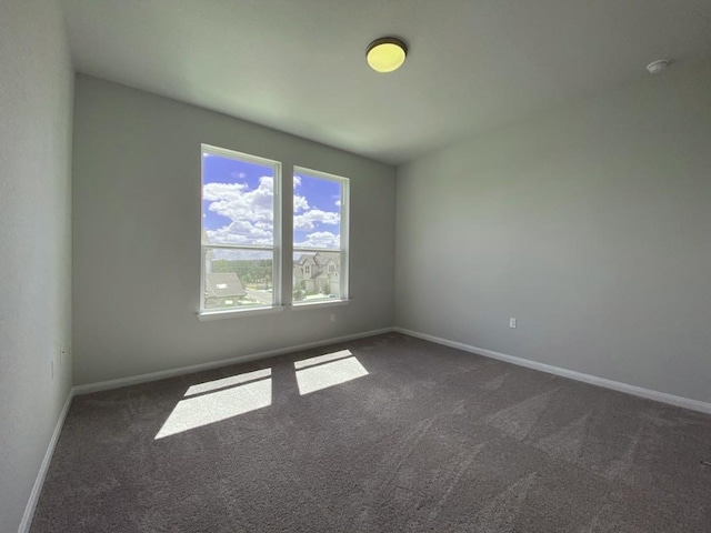 unfurnished room featuring dark colored carpet and baseboards