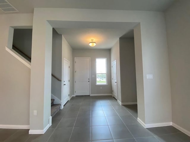 foyer featuring dark tile patterned flooring, baseboards, and stairs