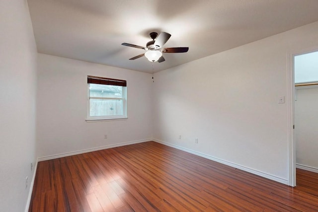 spare room featuring dark wood-type flooring, a ceiling fan, and baseboards