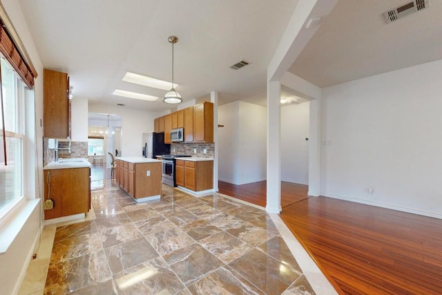 kitchen featuring stainless steel appliances, brown cabinetry, light countertops, and visible vents